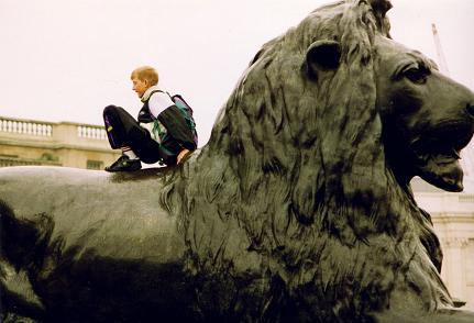 A child playing on top of a lion in Trafalger Square