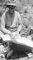 PALEONTOLOGIST, DR. DAVID WHITE IN THE CANYON WRAPPING FOSSIL IN NEWSPAPER FOR TRIP TO MUSEUM. CIRCA 1928. NPS, STURDEVANT