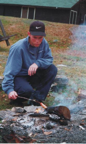 Tim roasting weiners on a campfire.