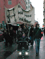 En funktionshindrad i permobil och en icke-funktionshindrad marcherar i ett demonstrationstg framfr en banderoll.