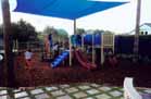 The Kids Play Area, behind the Community Centre.  Note the awning above to bring shade.  The area is fenced to keep the children out of the carpark.