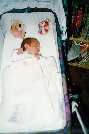 Nathan holding his Birth Certificate in his carry cot