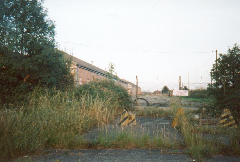(c.1996) a view of probably an original entrance to this part of the site, blocked off for quite sometime after a rearrangement. to the left of this photo is a small seperate fenced off area, with nothing inside. The yellow concrete pyramids are to stop people parking in this area. off in the far distance is the fuel tank.