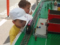 Boy in white cap with nose almost touching train; other boy behind him looking off in distance