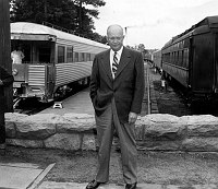GENERAL DWIGHT D. EISENHOWER STANDS BY STONE RAILHEAD WALL. 2 TRAINS BEHIND HIM. 17 JULY 1950 NPS PHOTO BY EDEN