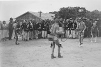 HOPI HOOP DANCERS WITH CHANTERS AT DESERT VIEW WATCHTOWER DEDICATION. DESERT VIEW HOUSE BEHIND (MOVED TO RESIDENTIAL AREA AFTER WATCHTOWER COMPLETED. MAY 13, 1933. FRED HARVEY CO. GRCA 22726<br>
