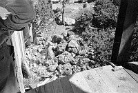 INSIDE WATCHTOWER DURING CONSTRUCTION. VIEW DOWN TO WORKER WHO IS HOISTING A LARGE BOULDER FOR WALL. CIRCA 1932. COLTER. 