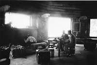 2 UNIDENTIFIED MEN SIT AT TABLE IN WATCHTOWER KIVA. WINDOW LIGHT. TEA SERVICE. CIRCA 1932. COLTER.
