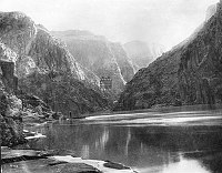 RUST TRAM CAGE & CABLE CROSSING COLORADO RIVER ABOVE MOUTH OF BRIGHT ANGEL CREEK. MAN WITH SMALL BOAT. CIRCA 1909. KOLB BROS.