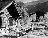 3 VISITORS SIT OUTSIDE ORIGINAL LODGE AT PHANTOM RANCH. VIEW TO S. SMALL COTTONWOOD TREES. CIRCA 1925. KEYSTONE STEREOGRAPH.