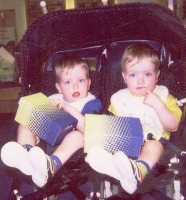 Two small boys in twin buggy are holding shoe boxes and looking inquisitive