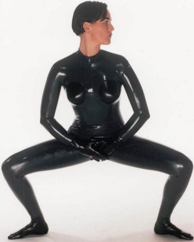 Great photograph of lithe Woman posing as defiant Vamp in tight black rubber outfit with gloves. 'Wicked Women in shiny catsuits' picture.